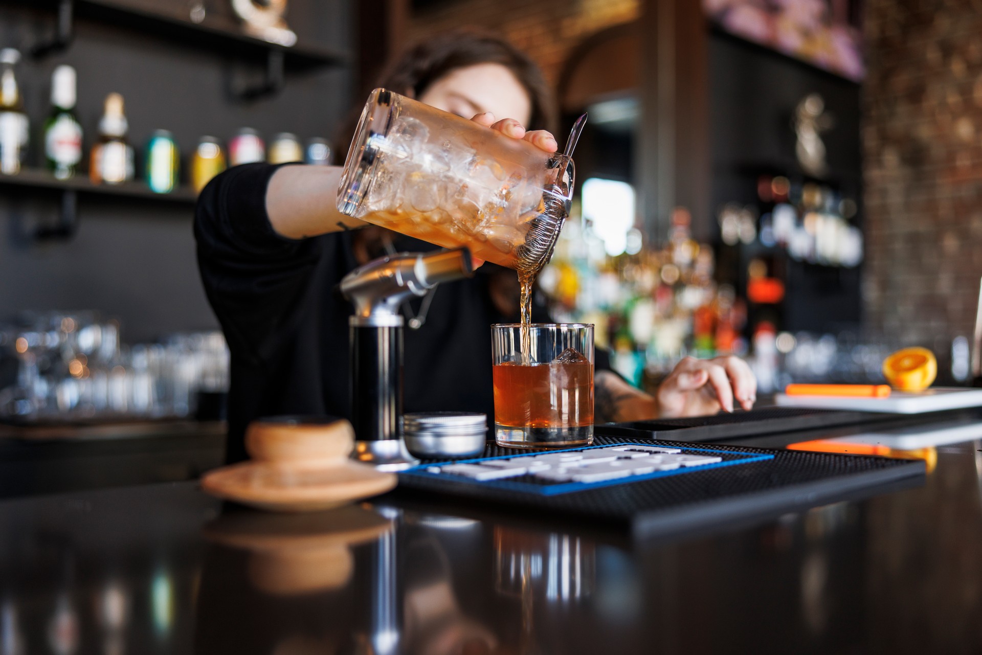 Smoked Old Fashioned cocktail crafted by female bartender, decanting and straining to the glass in a pub